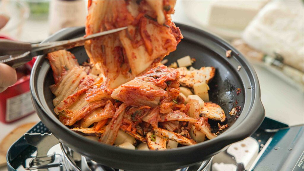 Cutting kimchi into pot of sauteed vegetables