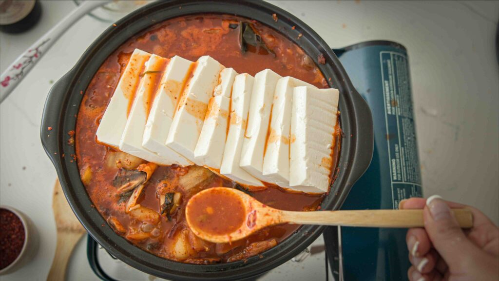 Tofu slices added to pot of boiling vegan kimchi jjigae