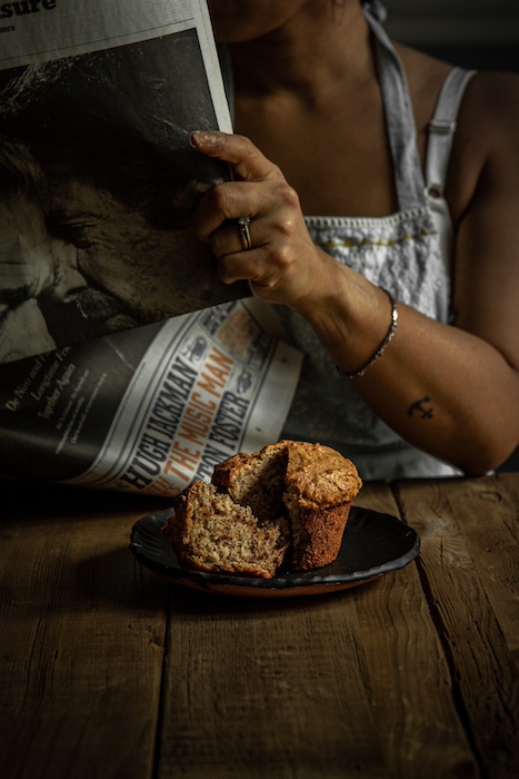 Joanne reading the newspaper while enjoying a Vegan Banana Chocolate Chip Muffin.