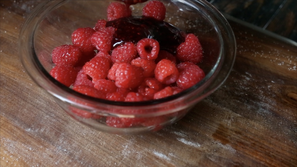 Adding melted raspberry preserves to fresh raspberries on your Vegan Berry Galette