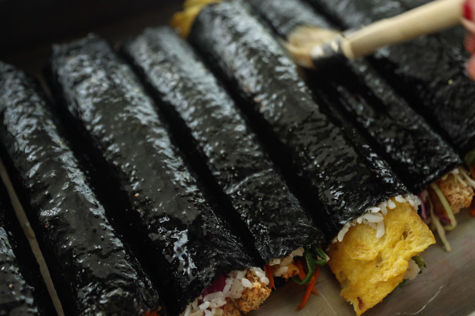row of kimbap rolls being brushed with sesame oil