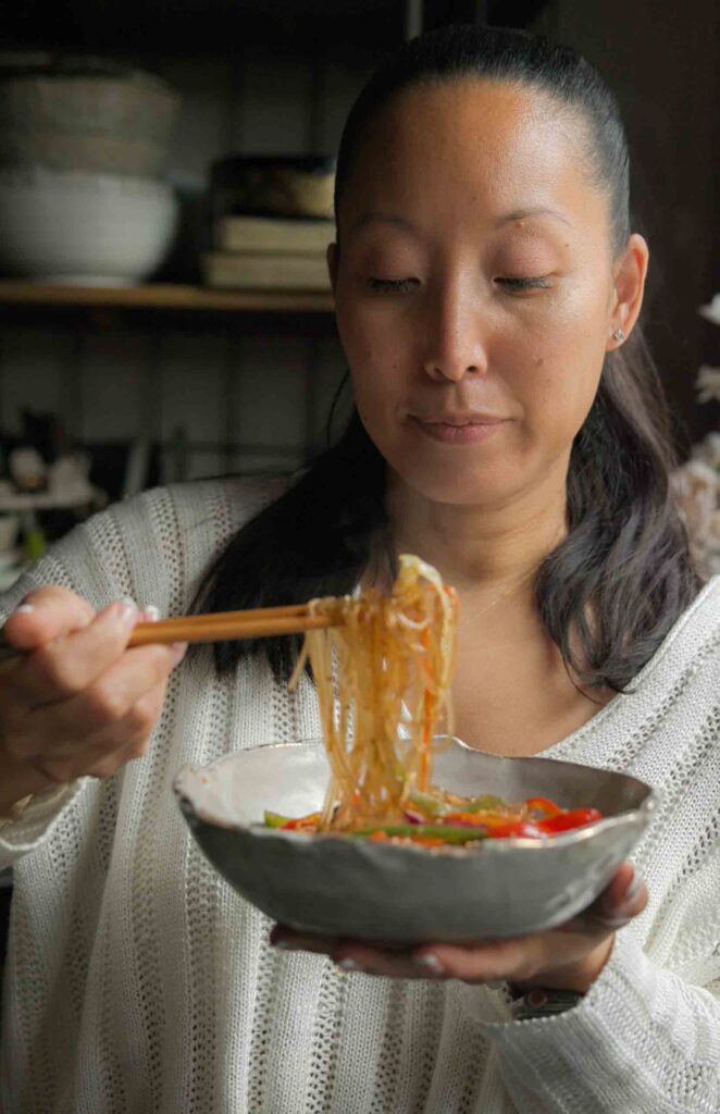 woman using chopsticks to eat vegan japchae
