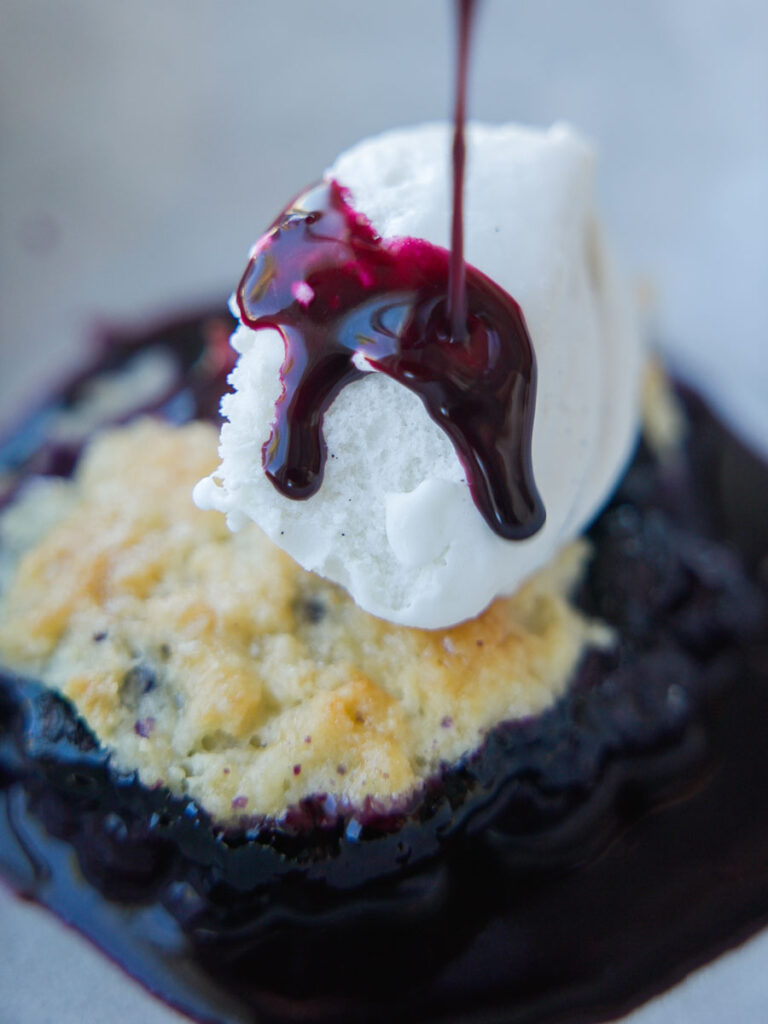 drizzling-blueberry-syrup-on-top-of-ice-cream-on-vegan-blueberry-cobbler.