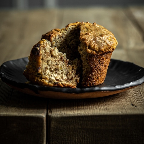 A single Vegan Banana Chocolate Chip Muffin sliced open on a plate.