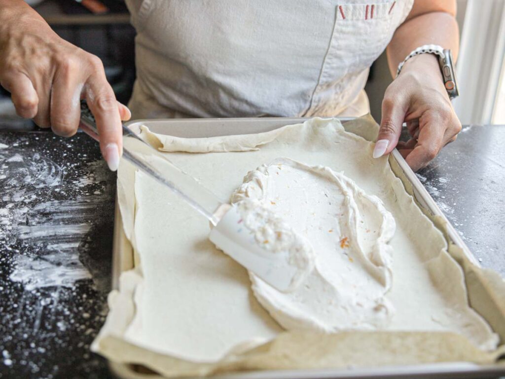 spreading-cream-cheese-filling-onto-peach-galette-pastry