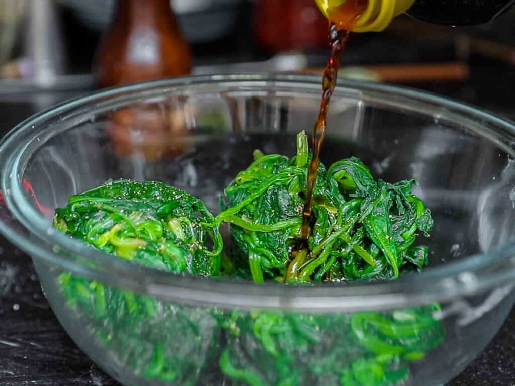 adding soy sauce to boiled spinach