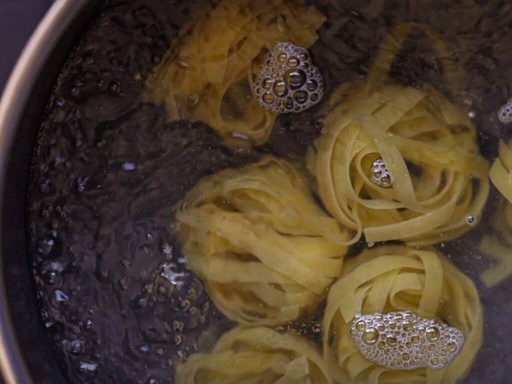 Tagliatelle pasta nests boiling in water, with bubbles forming around them in a pot.