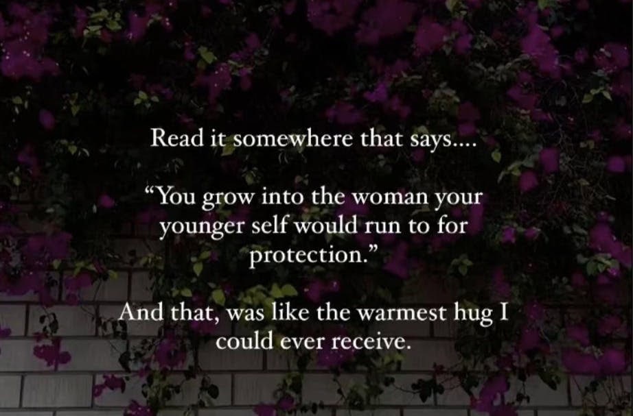 A wall covered with dark purple flowers and greenery. The text reads: Read it somewhere that says... You grow into the woman your younger self would run to for protection. It's like therapy language wrapped in the warmest hug I could ever receive.