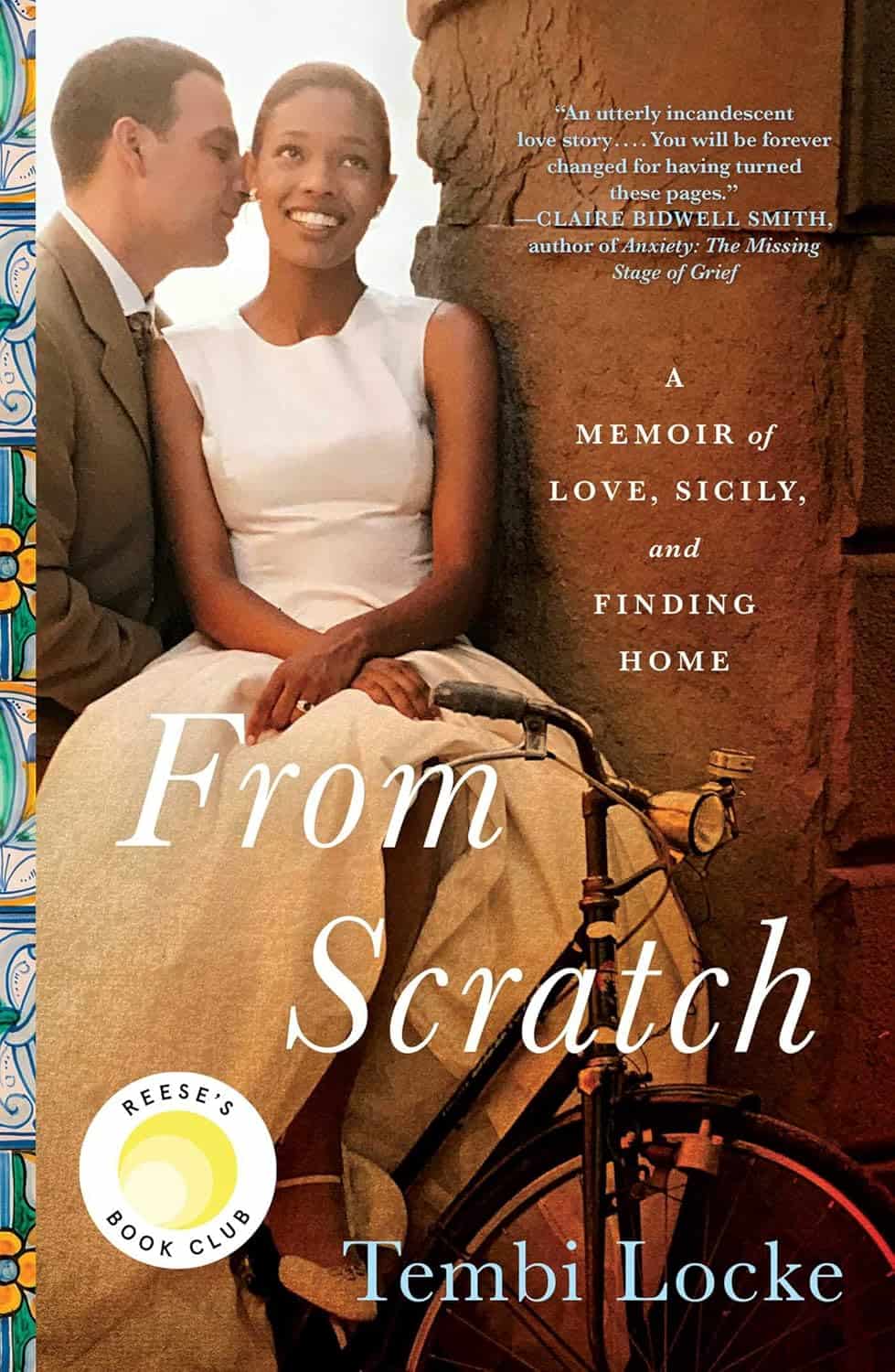 A couple sits closely together, smiling. The woman is in a white dress and the man in a suit, near a bicycle. The book cover reads, From Scratch: A Memoir of Love, Sicily, and Finding Home by Tembi Locke. With Reese's Book Club logo, it's an ideal addition to any 2024 Holiday Gift Guide.