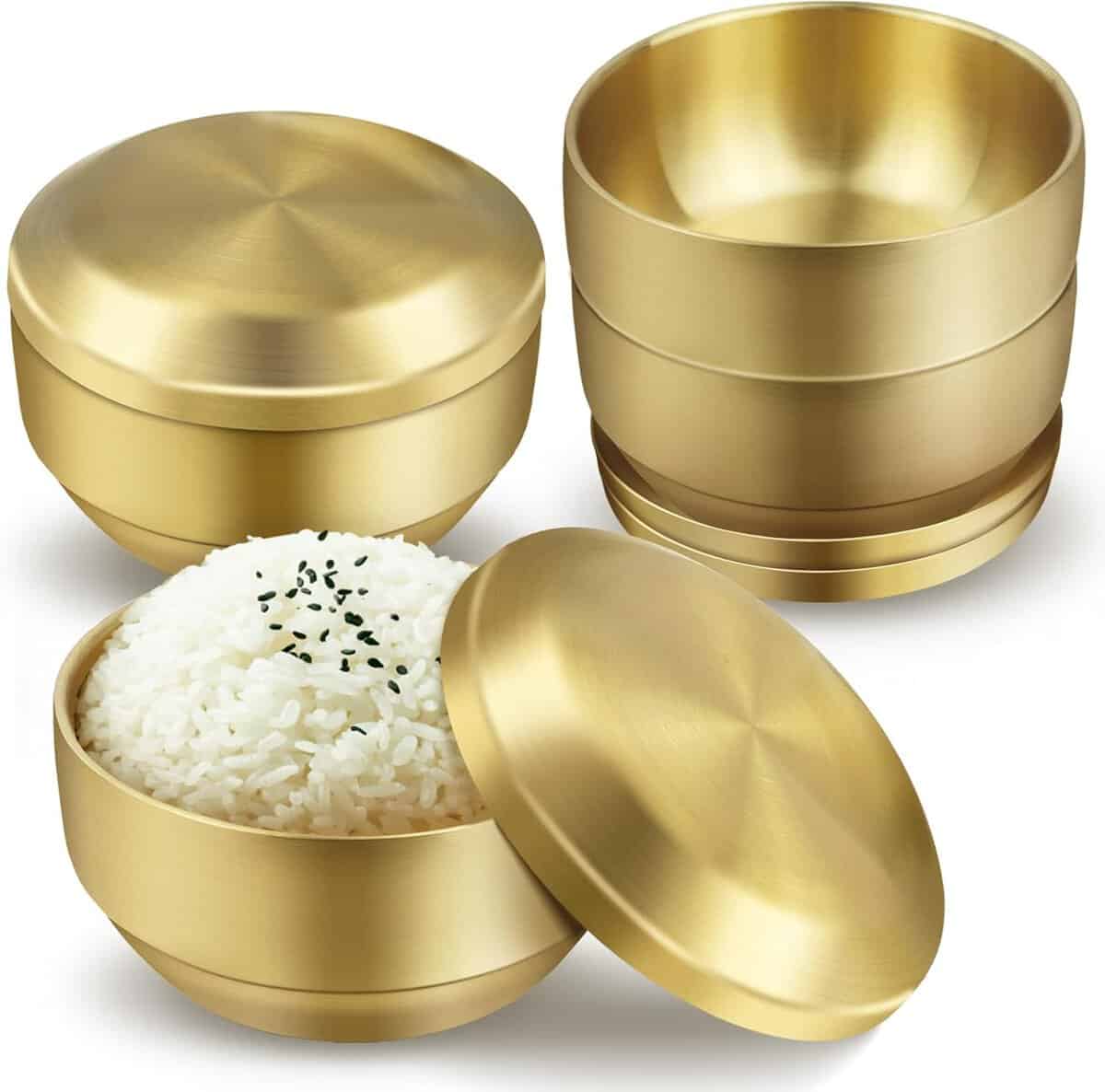 Shown are three gold-toned stainless steel bowls with lids, perfect as a stylish holiday gift. One bowl is filled with white rice garnished with black sesame seeds, while the others are stacked empty, showcasing their modern, sleek design.