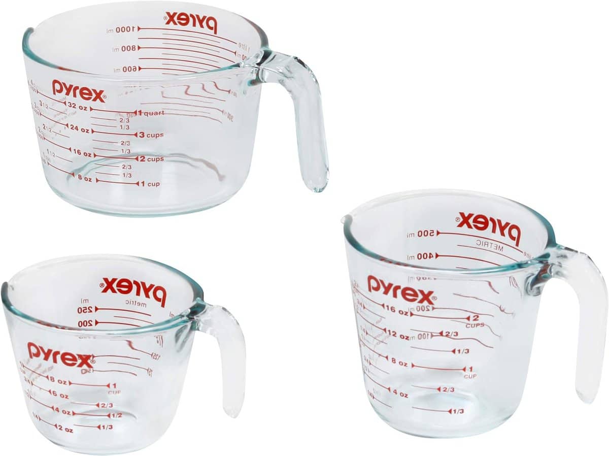 Three clear Pyrex glass measuring cups with red markings, showing various measurements in cups, ounces, and milliliters. Featured in the 2024 Holiday Gift Guide, these essentials rest elegantly on a white background.