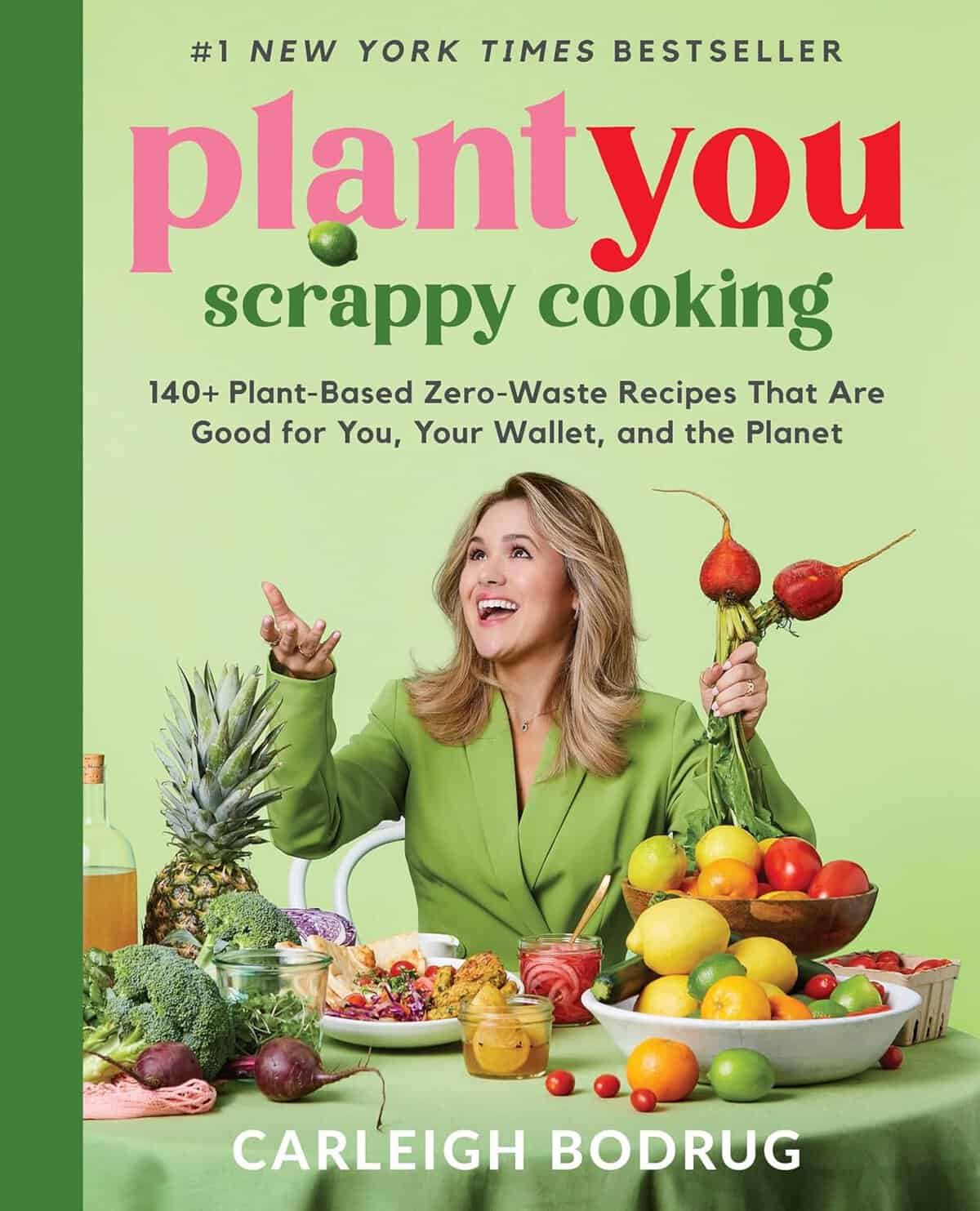 Cover of the book Plant You: Scrappy Cooking by Carleigh Bodrug. Perfect for the Holiday Gift Guide 2024, it features the author smiling, surrounded by an array of fruits and vegetables. The subtitle highlights plant-based, zero-waste recipes.