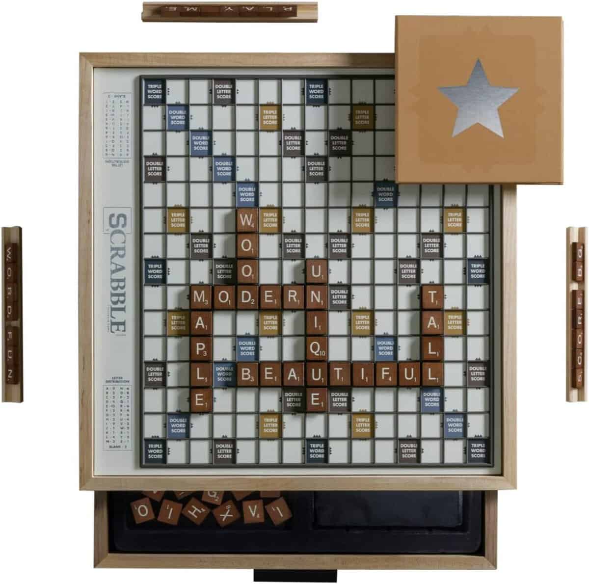 A Scrabble board features words like WOODEN, MODERN, BEAUTIFUL, MAPLE, UNIQUE, and TALL with brown wooden tiles. A box with a silver star sits nearby.