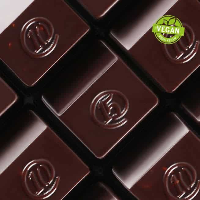 Close-up of dark chocolate squares with embossed logos, arranged neatly. In the top right corner, a green Vegan label proudly certifies them as part of the 2024 Korean Vegan Holiday Gift Guide.