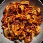30+ AMAZING VEGAN Holiday Recipes Everyone's gonna Love. 12 A bowl of wide, ribbon-like pasta topped with chunky vegan bolognese sauce, garnished with chopped herbs, and served on a gray plate.