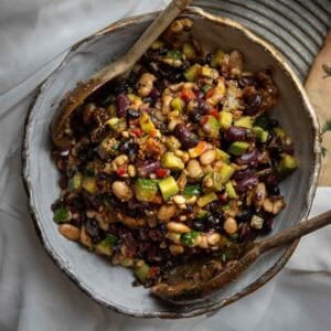 A bowl of colorful Korean BBQ dense bean salad with kidney beans, white beans, black beans, diced vegetables, and herbs, mixed and served with wooden salad utensils on a rustic plate.