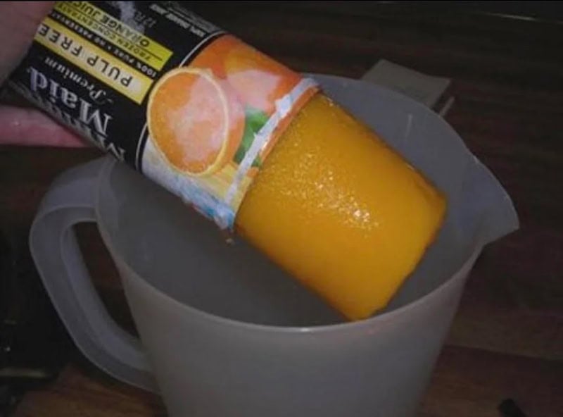 A frozen cylinder of orange juice concentrate is being slid out of its cardboard can into a plastic pitcher on a kitchen counter by a little brother eager for a treat, his excitement reminiscent of hearing the distant chime of an ice cream truck.