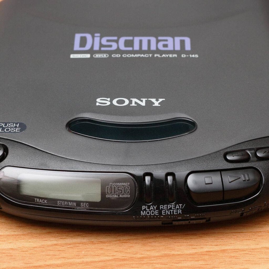 Close-up of a black Sony Discman portable CD player, showing the display screen and control buttons as it sits on a wooden surface—just like the one my little brother used to carry when chasing after the ice cream truck.
