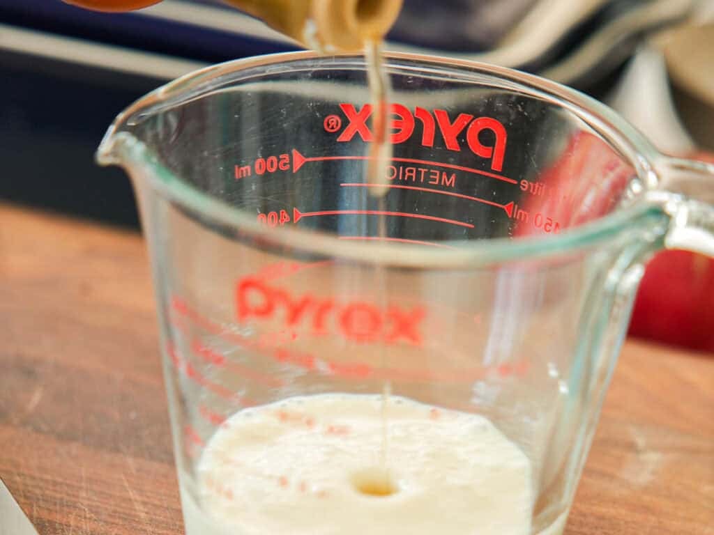A close-up of vinegar being poured into a Pyrex measuring cup on a wooden surface, with measurement markings visible on the glass.