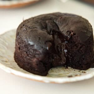 A close-up of a vegan chocolate lava cake on a plate, with rich, melted chocolate oozing from the center of the moist, dark cake.