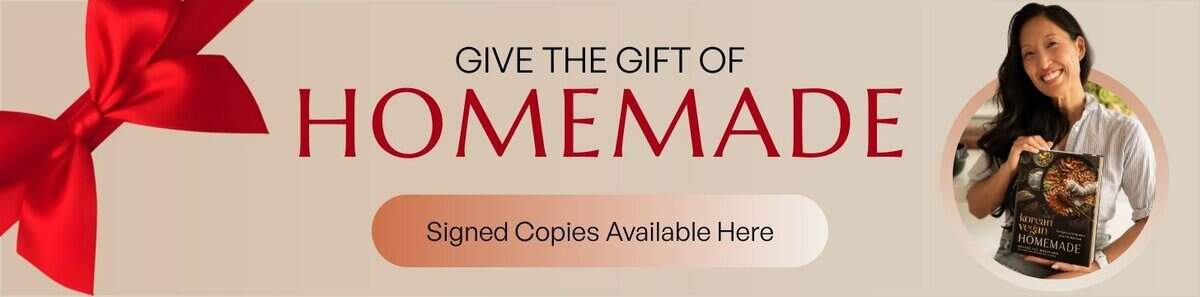 Banner with a large red ribbon and bow on the left. Text reads Give the gift of HOMEMADE. Signed copies available here. On the right, the author, Joanne Lee Molinaro, holds a cookbook titled HOMEMADE.