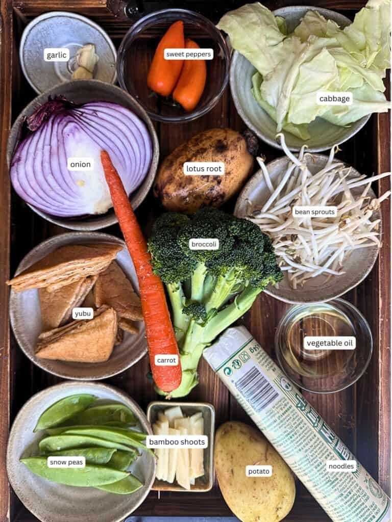Easy & Healthy Lo Mein Vegan Recipe: Done in Minutes. 22 A tray with labeled bowls of garlic, sweet peppers, cabbage, onion, lotus root, bean sprouts, yubu, carrot, broccoli, vegetable oil, snow peas, bamboo shoots, potato, and noodles.