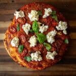 30+ AMAZING VEGAN Holiday Recipes Everyone's gonna Love. 6 A homemade focaccia rossa topped with tomato sauce, roasted tomato slices, dollops of ricotta cheese, and fresh basil leaves, shown on a wooden surface.