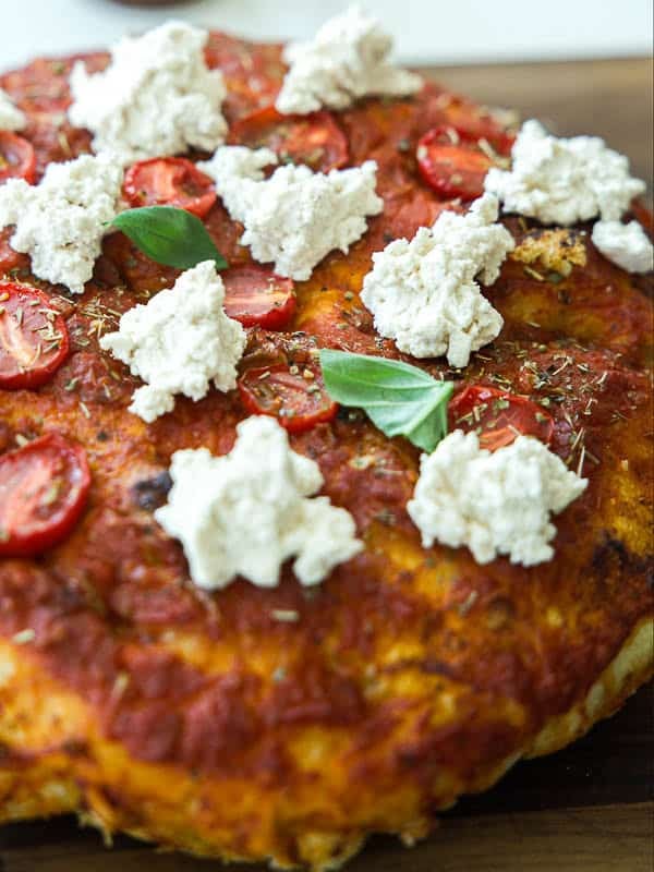close up shot of focaccia rossa with dollop of vegan ricotta and fresh basil