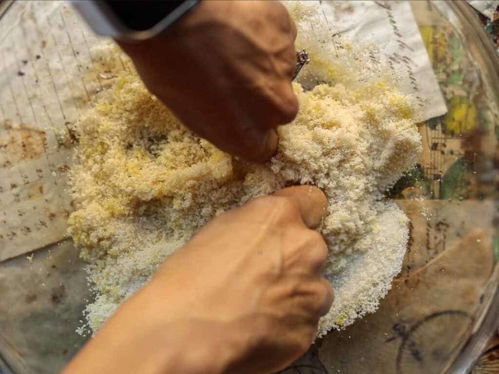 a woman using her hands to massage the sugar into the lemon zest.