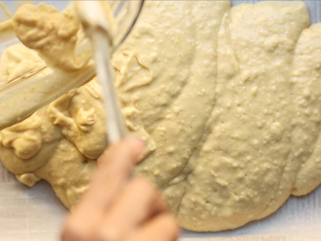 pouring lemon cake batter onto baking sheet lined with parchment paper.