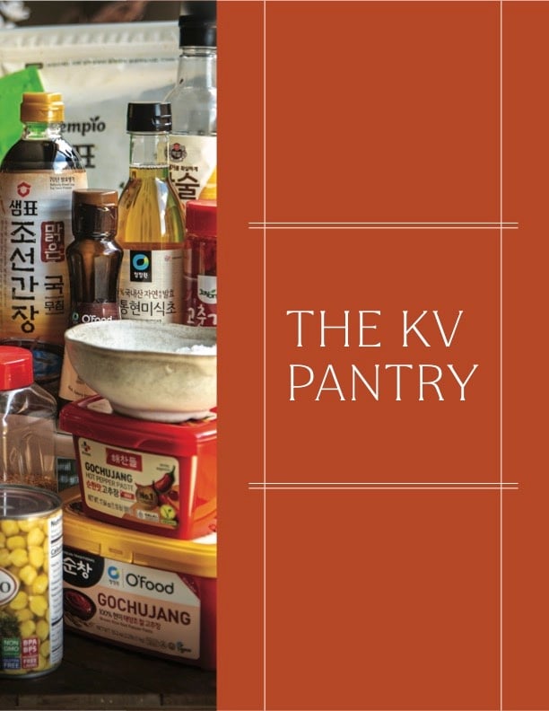 A variety of Korean pantry staples, including sauces, canned corn, and condiments, arranged on a counter beside a red panel that reads THE KV PANTRY in white text—perfect for your next Book PreOrder cooking adventure.