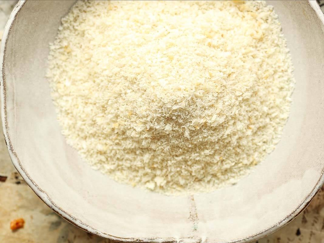 A close-up of a bowl filled with light, flaky panko breadcrumbs, shown from above. The bowl has a rustic, textured look and sits on a neutral-colored surface.