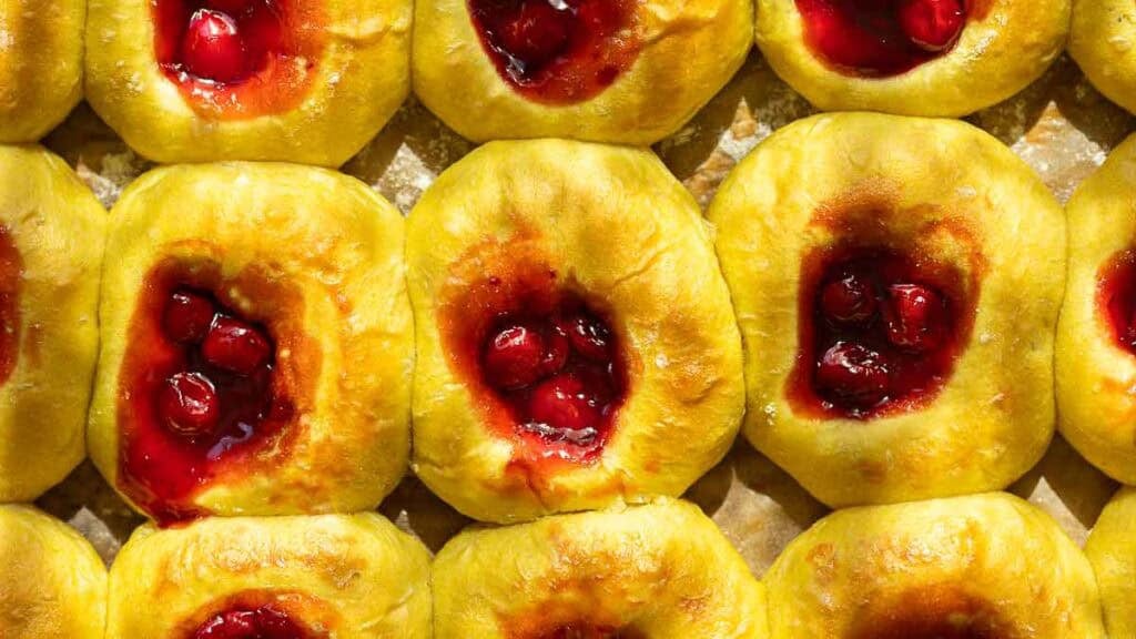 Easy Cherry Brioche Sweet Roll - Vegan Pastry. 17 Rows of golden cherry brioche sweet roll with centers filled with glossy red cherry filling, displayed close together on a baking sheet.