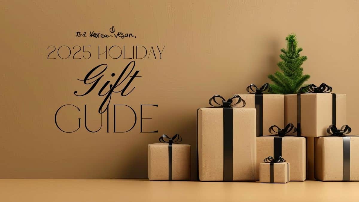 A minimalist holiday scene with beige gift boxes tied with black ribbons stacked beside a small green fir tree. Text reads “The Korean Vegan 2025 Holiday Gift Guide.”