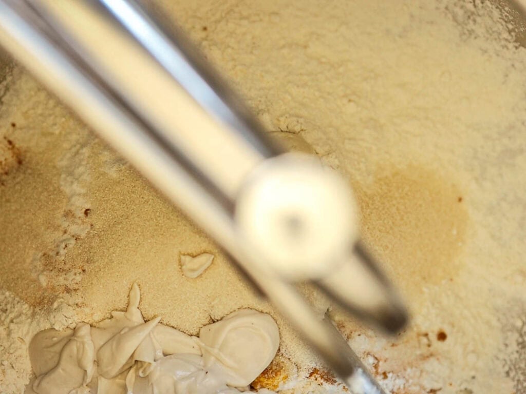 Easy Cherry Brioche Sweet Roll - Vegan Pastry. 22 A close-up view of a mixing bowl containing flour, a dollop of vegan yogurt, and a metal beater from a mixer partially visible in the foreground.