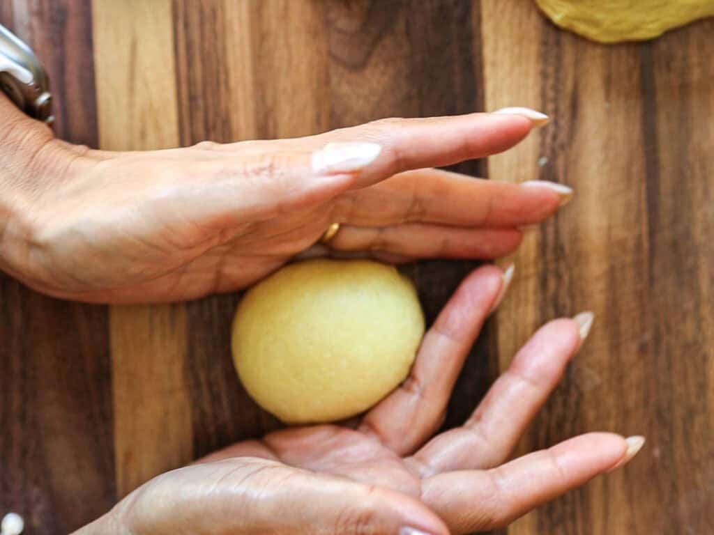 Easy Cherry Brioche Sweet Roll - Vegan Pastry. 27 Two hands shaping a ball of dough on a wooden surface, preparing it for baking.