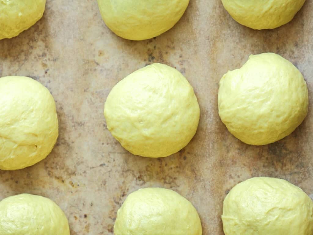 Easy Cherry Brioche Sweet Roll - Vegan Pastry. 29 Eight round balls of yellow dough are evenly spaced on a parchment-lined baking sheet, ready for baking.