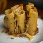 30+ AMAZING VEGAN Holiday Recipes Everyone's gonna Love. 10 Close-up of a serving of baked mushroom rigatoni pie filled with a cheesy, mushroom mixture, topped with melted cheese and herbs, on a white plate.
