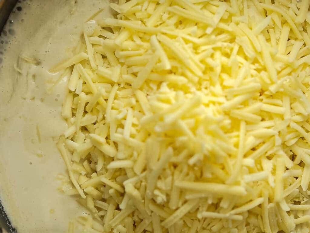 A close-up of a pile of shredded cheese on top of a creamy sauce, ready to be mixed together.