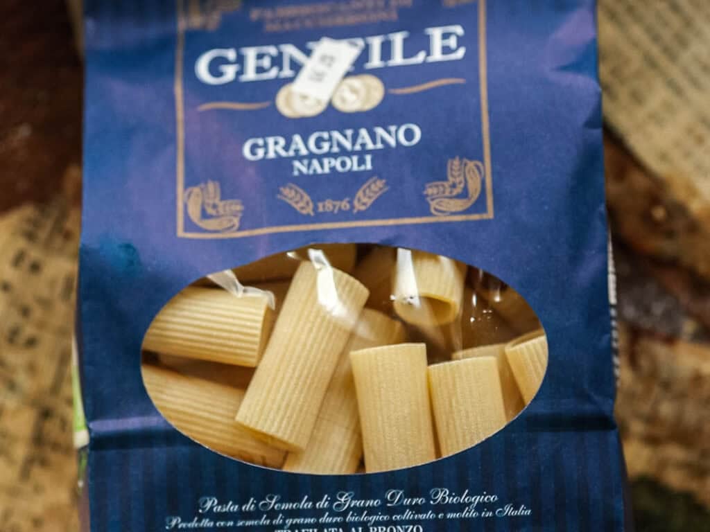 A blue package of Gentile Gragnano Napoli pasta with a clear window showing tube-shaped pasta inside. The label indicates it is organic durum wheat pasta made in Italy.