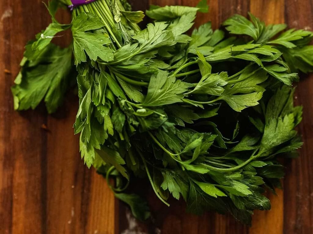 A bunch of fresh parsley with green leaves sits on a wooden surface.