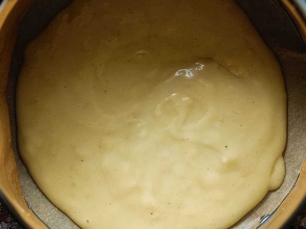 A close-up of thick, creamy béchamel spread evenly in a round, parchment-lined baking tin, ready to be baked.