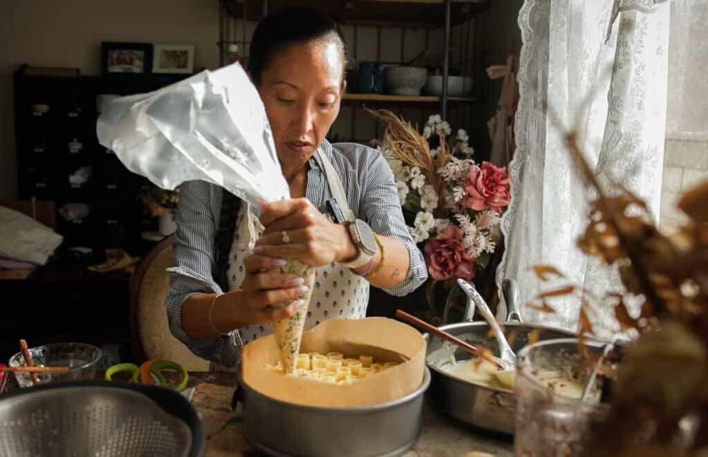 a woman piping ricotta mixture into springform pan of upright rigatoni.