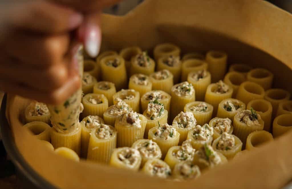 someone piping in ricotta filling into upright rigatoni.