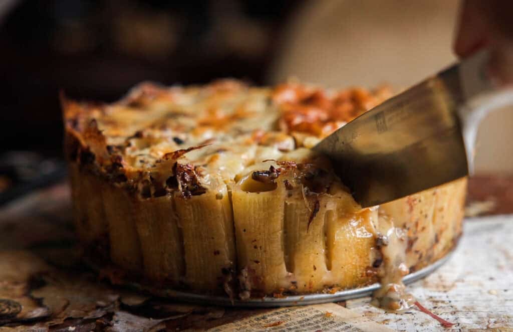 someone slicing mushroom rigatoni pie