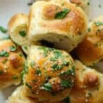 30+ AMAZING VEGAN Holiday Recipes Everyone's gonna Love. 2 A close-up of golden, fluffy garlic knots recipe topped with chopped parsley and sprinkled with grated cheese, showing a soft, airy interior and a shiny, buttery surface.