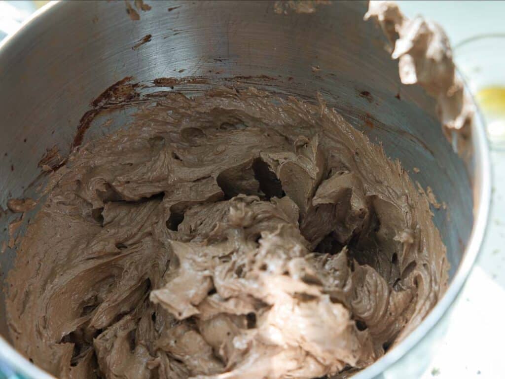 The BEST Vegan Chocolate Cake Recipe On The Internet. 29 A metal mixing bowl filled with thick, creamy frosting, partially mixed, with some sticking to the sides of the bowl.