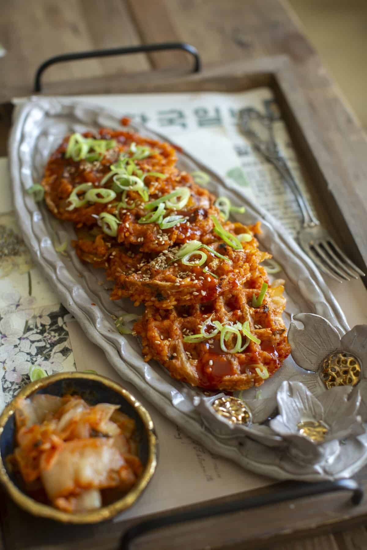 10+ Delicious and Easy Recipes Using Kimchi Today! 15 A decorative plate holds crispy Korean kimchi pancakes topped with sliced green onions and sesame seeds, served on a wooden tray with a small bowl of kimchi—an irresistible choice for fans of delicious kimchi recipes.