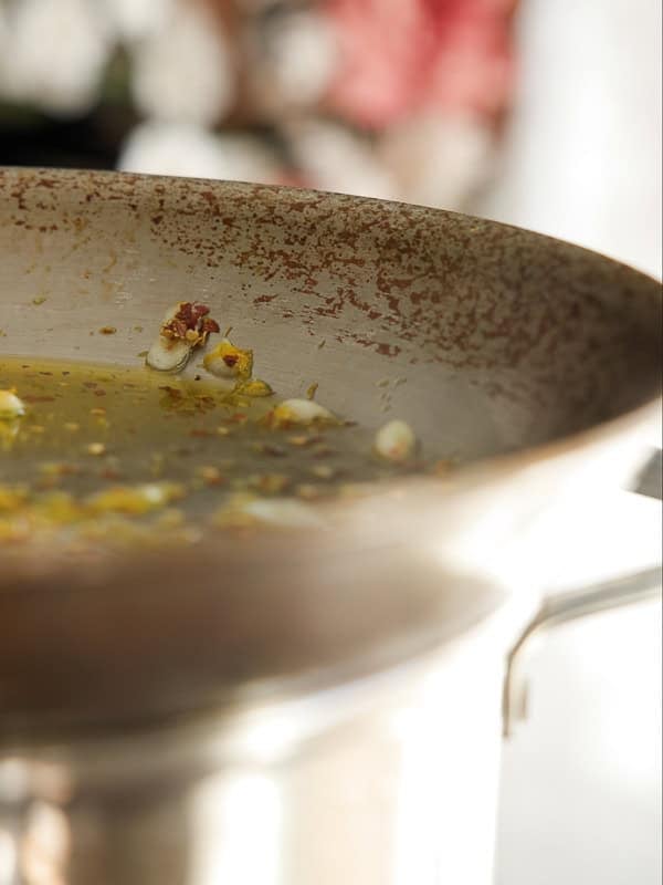 8-ingredient Easy and Delicious Lemon Pepper Pasta. 7 A close-up of a metal pot with hot oil and a few popped popcorn kernels floating on the surface, much like preparing the start of an easy pasta recipe. The blurred background draws focus to the edge and contents of the pot.