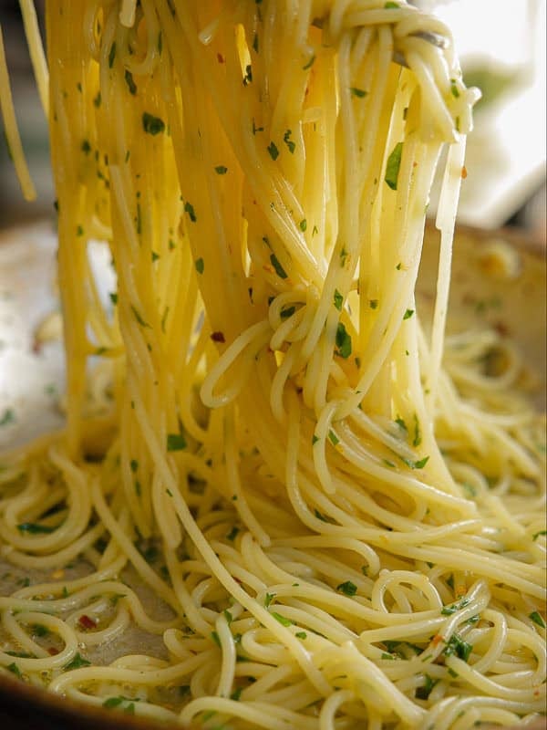 8-ingredient Easy and Delicious Lemon Pepper Pasta. 16 Close-up of delicious pasta being lifted from a pan, garnished with chopped parsley and glistening with olive oil for an easy pasta dish.